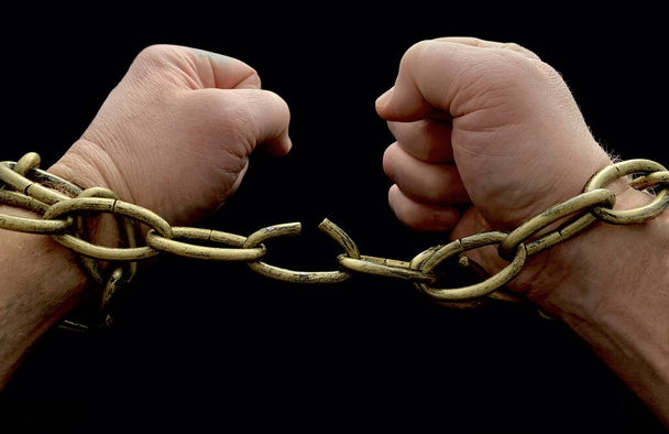 Мужские руки разорвали цепь, на черном фоне. Человек прикован цепями, у него связаны руки. Понятие свободы, рабства
. - Фото, изображение