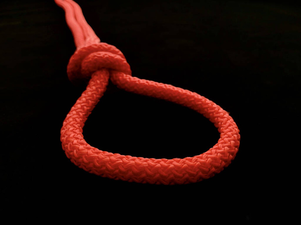 Loop of bright rope, on a black background. The rope is tied in a loop with a knot. - Фото, изображение
