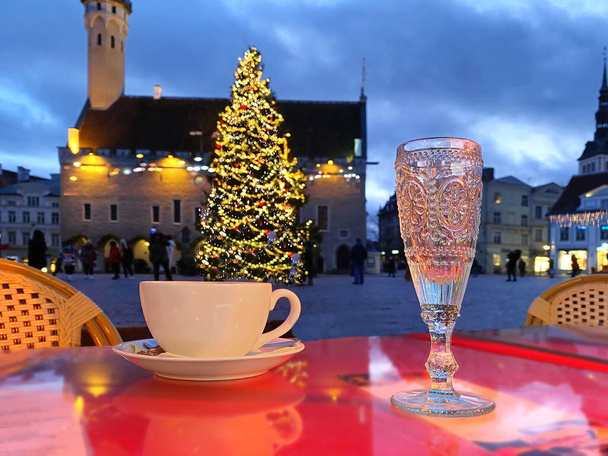 Noel 'de şehir bayramında yeni yıl ışığı, masa başında bir fincan kahve ve Tallinn caddesindeki kafede mavi bir kadeh şarap, ağaç süsleme ışıkları bulanıklaşıyor, insanlar yürüyor, en iyi şenlikli kış pazarı, Estonya' ya tatil seyahati - Fotoğraf, Görsel