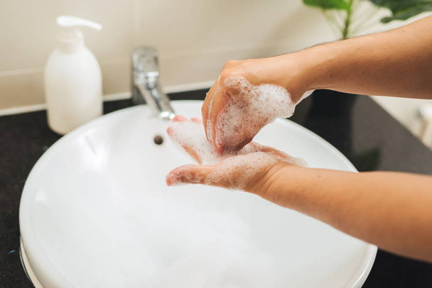Concepto de higiene. El hombre se lava las manos en el baño con jabón bajo el agua corriente
. - Foto, imagen