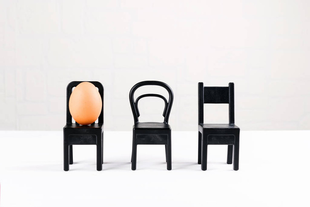 Um ovo está sentado numa cadeira preta. Design de ideias de negócios. Conceito de individualidade, exclusividade. Ideia de conceito de Páscoa mínima
 - Foto, Imagem