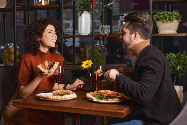 Nuori pariskunta syö pizzaa pizzeriassa. Mies huvittaa tyttöään ravintolassa. Onnelliset ihmiset pitävät hauskaa yhdessä
 - Valokuva, kuva