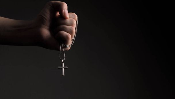 Close-up images of crucifix pendant necklace in man hand on black color background in studio which represent praying for god or jesus and thank gods for giving peaceful and faithful to people - Foto, Imagem