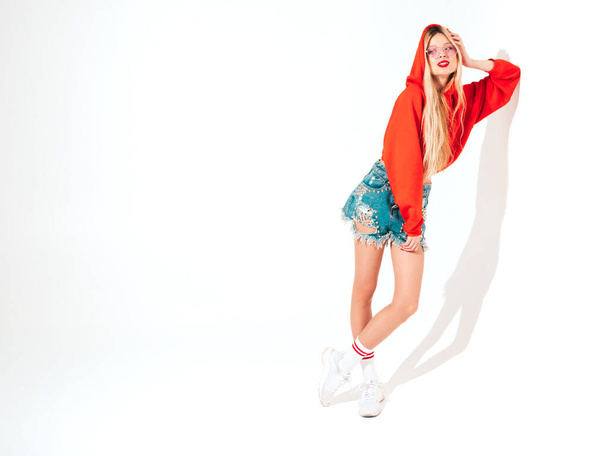 Portrait of young beautiful hipster bad girl in trendy red summer hoodie and earring in her nose.Sexy carefree smiling blond woman posing in studio.Positive model having fun.Isolated on white  - Φωτογραφία, εικόνα