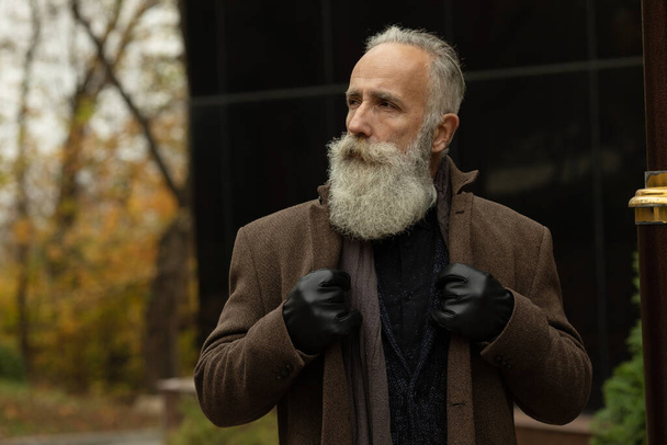 Fashionable senior man with gray hair and beard is outdoors on the street. - Foto, Imagen