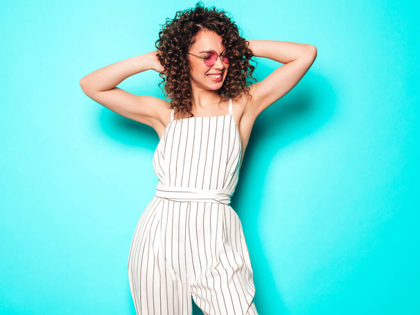 Portrait of beautiful smiling model with afro curls hairstyle dressed in summer hipster clothes.Sexy carefree girl posing in studio near blue wall.Trendy funny and positive woman - Photo, image