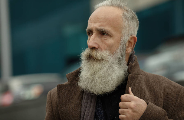 Fashionable senior man with gray hair and beard is outdoors on the street. - Zdjęcie, obraz