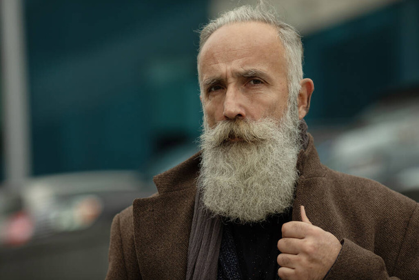 Μοντέρνος ηλικιωμένος άνδρας με γκρίζα μαλλιά και γενειάδα είναι έξω στο δρόμο. - Φωτογραφία, εικόνα