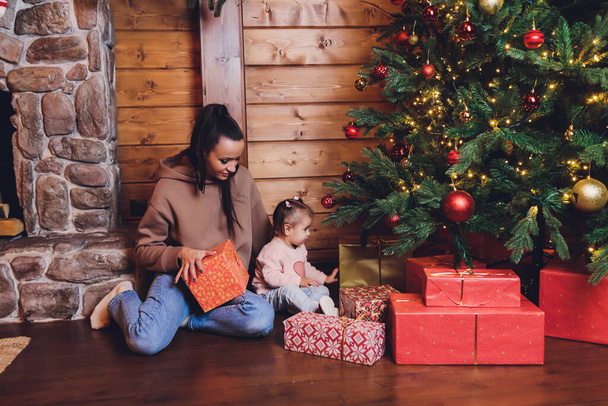 Merry Christmas and Happy Holidays Cheerful mom and her cute daughter girl exchanging gifts. Parent and little child having fun near Christmas tree indoors. Loving family with presents in room. - Фото, зображення