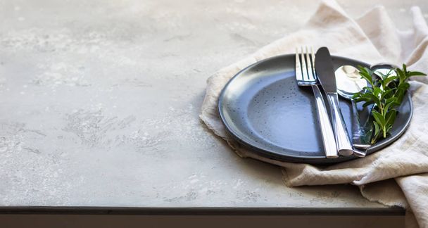 Elegant table setting with black ceramic plate, cutlery and canvas napkin on grey stone background. Space for text. - Фото, зображення