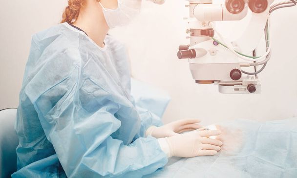 Tratamento Lasik. Correcção da visão laser. Médico examina fundo em microscópio, paciente sob cobertura estéril
. - Foto, Imagem