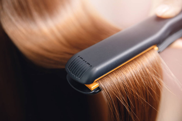 Hair iron in hand of master straightens with keratin - Photo, Image