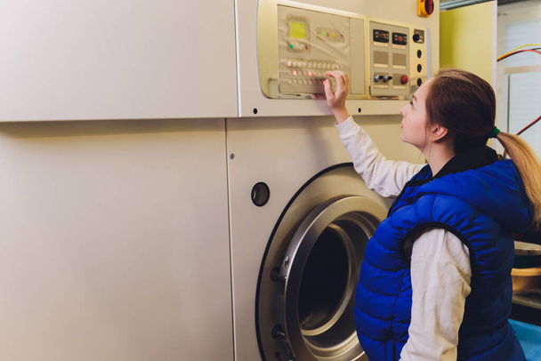 Mujer joven presionando botones en la lavadora en la limpieza en seco
. - Foto, imagen
