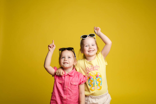 Two happy beautiful stylish little girl wearing sunglasses posing isolated yellow studio background - Foto, Bild