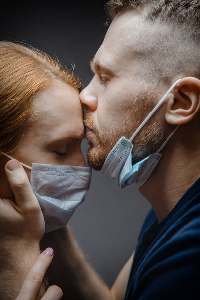 Liebhaber Mann und Mädchen küssen sich in Schutzmasken Atemschutzmaske auf dunklem Hintergrund, Menschen betroffen epidemischen Virus, verbreiten Tröpfchen in der Luft - Foto, Bild