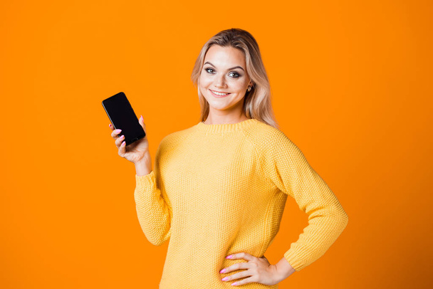 Cute young woman in a yellow sweater holding a smartphone - Foto, imagen