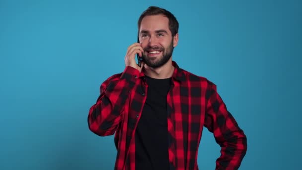 Young man in red wear talking on mobile phone on blue background. Trendy guy have conversation. Smartphone, technology concept. - Filmmaterial, Video