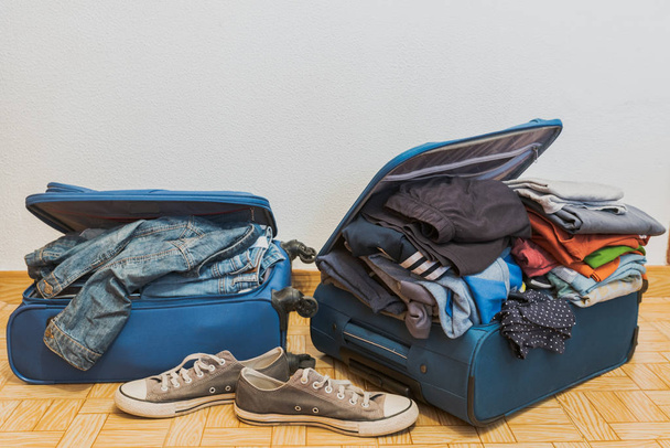 χαοτική μπλε βαλίτσα με πολλά ρούχα, προετοιμασία για διακοπές, λευκό φόντο - Φωτογραφία, εικόνα