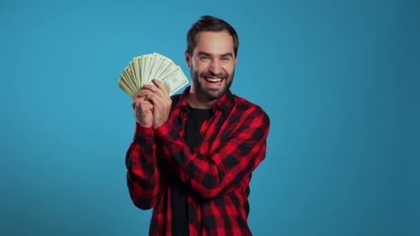 Satisfied happy excited man showing money - U.S. currency dollars banknotes on blue wall. Symbol of success, gain, victory. - Filmagem, Vídeo