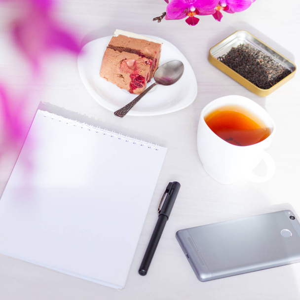 Xícara de chá, flores, caderno de papel sobre fundo branco. Edição de textos, conceito freelance
. - Foto, Imagem