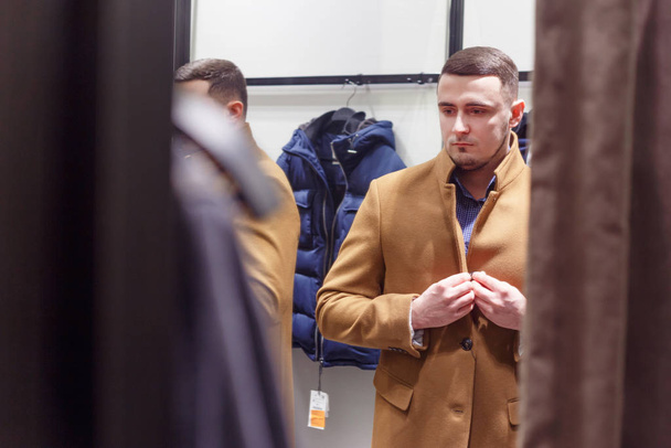 30 ans homme essayant sur un manteau classique brun automne dans une salle d'essayage, vente de collection. - Photo, image