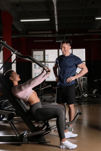 Trainer with young woman working out on chest press machine in g - 写真・画像