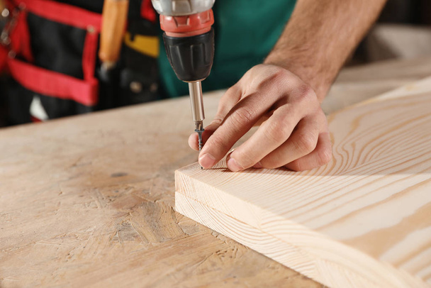 Professional carpenter twisting screw with drill at workbench, closeup - Φωτογραφία, εικόνα