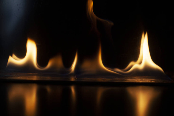 Fiery background. Flames of fire in the dark. Flame texture. Tongues of fire rise smoothly. A simple background of yellow shades. Burning gel for ignition. Ignition of vapors. Fire is danger. - Fotoğraf, Görsel