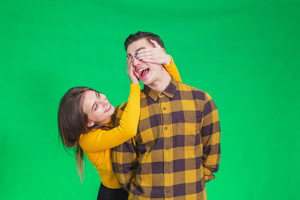 Playful girl covering boyfriends eyes with hands on green background. - Fotoğraf, Görsel
