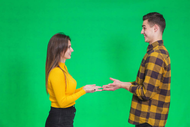 Confused millennial couple isolated on green studio background shrug shoulders feel doubtful and hesitant about something they hold in hands. - Фото, изображение