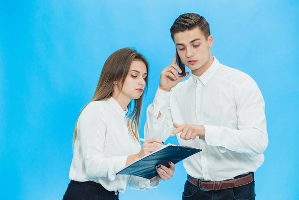Portrait of handsome businessman speaking on phone and his secretary making notes over blue background. - Photo, Image