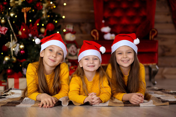 Κορίτσια με κόκκινα καπέλα ονειρεύονται δώρα στο φόντο του Χριστού - Φωτογραφία, εικόνα