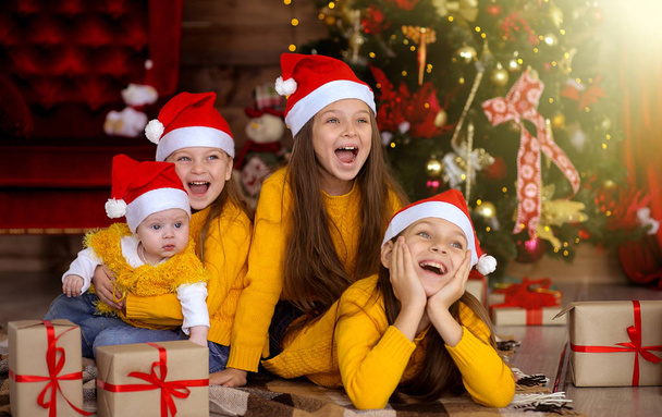 Kinder lächeln mit roten Hüten auf dem Hintergrund des Weihnachtsfestes  - Foto, Bild