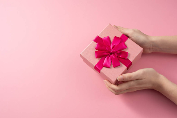Valentine's Day celebration concept. A nice gift from a loved one. Box with a bow in female hands on a delicate pink background. Copy space. Flat lay. - Valokuva, kuva