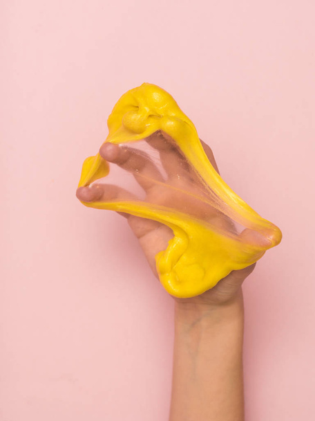 Yellow slime stretched on the palm of your hand on a pink background. - Φωτογραφία, εικόνα
