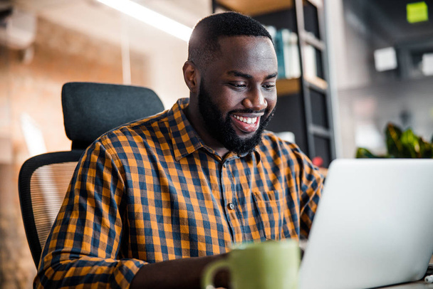 Positive delighted dark-skinned man staring at his laptop - Foto, imagen