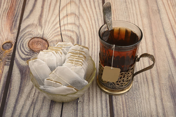 Chá em um copo facetado em um porta-copos vintage e sacos de chá em um vaso de vidro em um fundo de madeira. Fechar
. - Foto, Imagem