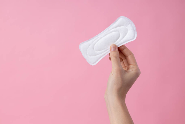 Holding menstrual pad in fingers on pink background stock photo - Fotoğraf, Görsel