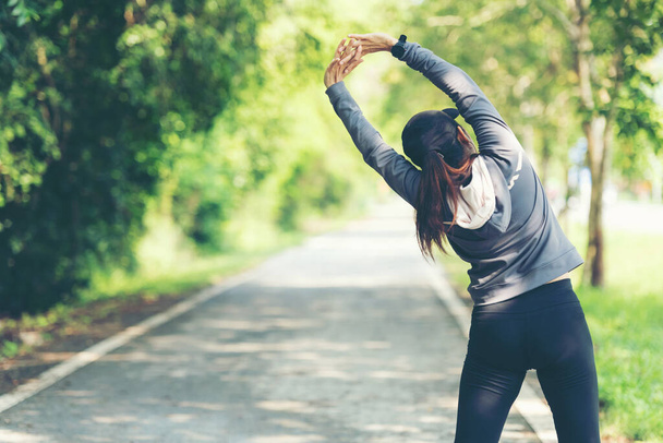 Healthy woman warming up before jogging run and relax stretching her arms and looking away in the road outdoor. Asian runner people workout fitness session, nature park background. Healthy and Lifestyle Concept. - Фото, зображення