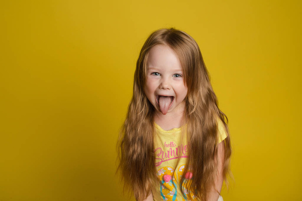 Portrait of beautiful little girl with long hair smiling posing isolated at yellow studio background - Photo, Image