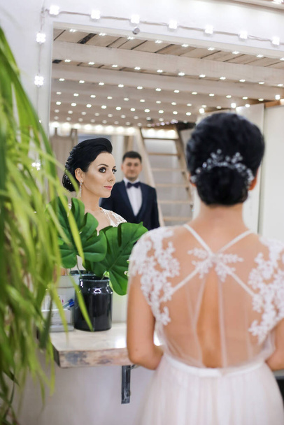 ヘアスタイルとウェディングドレスを着た花嫁が鏡を見て - 写真・画像