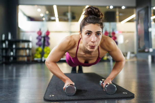 Женщина делает отжимания упражнения с гантели в фитнес-тренировки
 - Фото, изображение