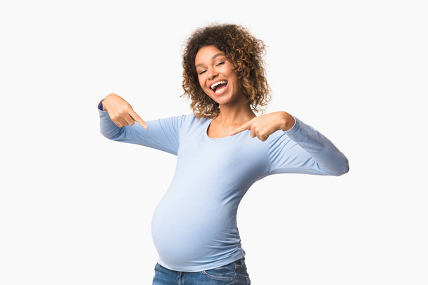 Emotional pregnant woman smiling and pointing fingers at belly - 写真・画像