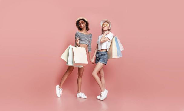 Дві стильні дівчата з сумками для покупок позує на рожевому тлі
 - Фото, зображення