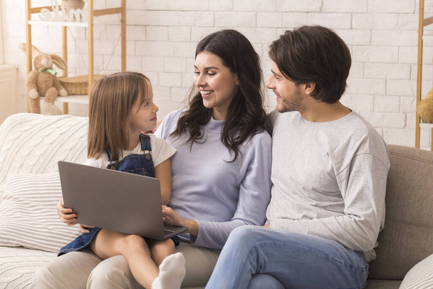 Portrait of young parents and their little daughter using laptop together - Photo, Image