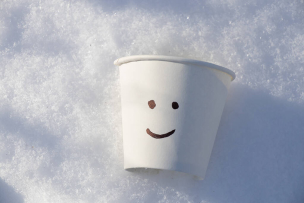 a paper white glass in the snow and a smile is painted on it - Photo, Image