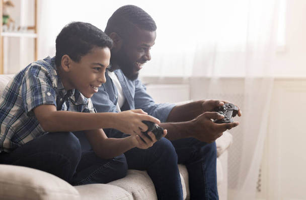 Afro father and son playing video games with joysticks - Photo, image