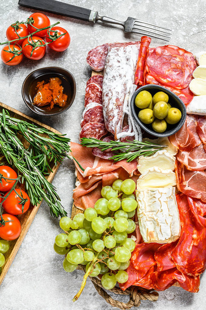 Italian antipasto, wooden cutting board with prosciutto, ham, parma, goat and Camembert cheese, olives, grapes. antipasti. Gray background. Top view - Photo, Image