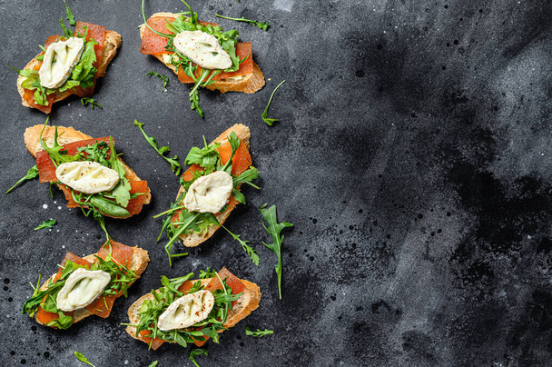 bruschetta with goat cheese, arugula and pear marmalade. Black background. Top view. Copy space - Фото, изображение