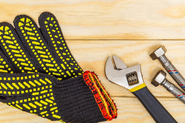 Plumbing equipment repair tools adjustable wrench and hose, gloves, flexible connection on wooden boards - 写真・画像